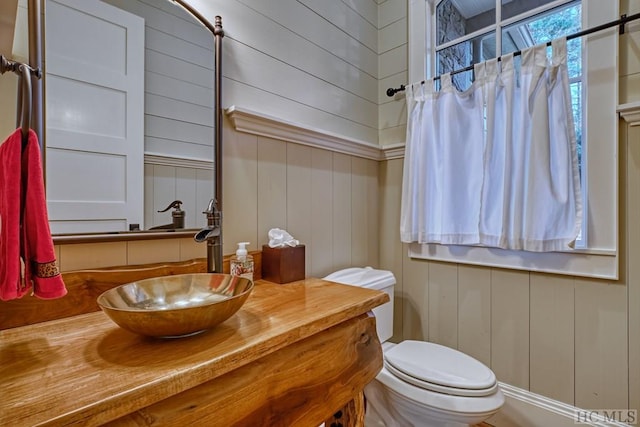 bathroom featuring vanity, wooden walls, and toilet