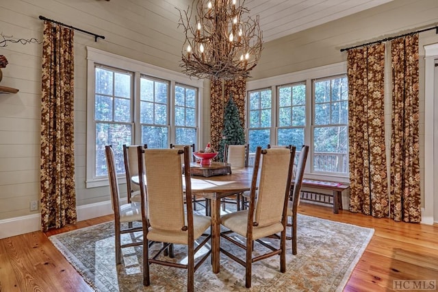 dining room with light hardwood / wood-style floors, a notable chandelier, wood walls, and a wealth of natural light