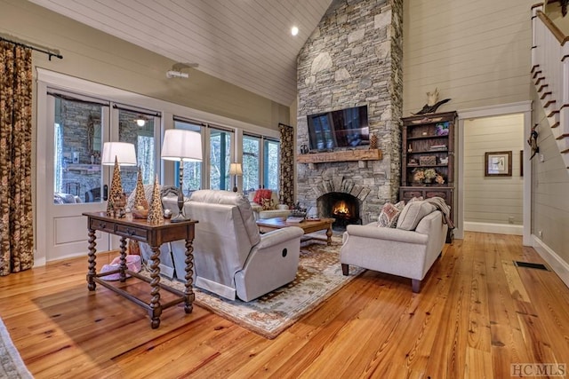 living room featuring wood ceiling, light hardwood / wood-style flooring, wooden walls, high vaulted ceiling, and a stone fireplace