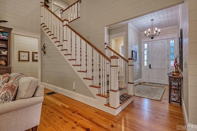 foyer entrance with crown molding, wood walls, an inviting chandelier, and light hardwood / wood-style flooring