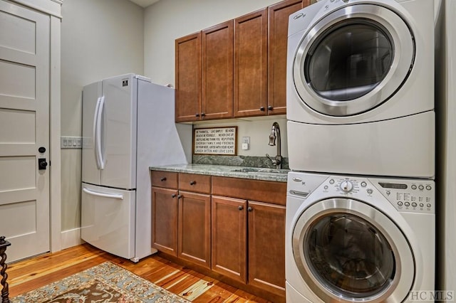 clothes washing area with cabinets, stacked washer and clothes dryer, sink, and light wood-type flooring