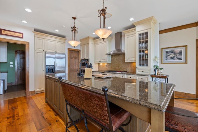 kitchen with wall chimney exhaust hood, a breakfast bar area, a large island with sink, and glass insert cabinets