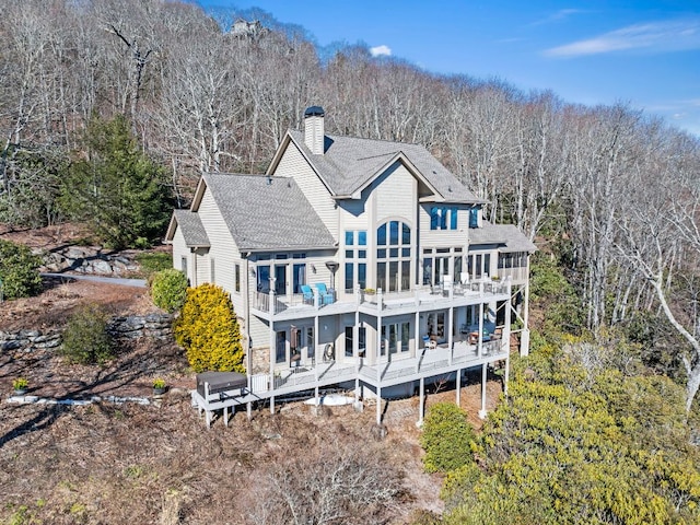 rear view of property featuring a shingled roof, a chimney, a deck, and a balcony