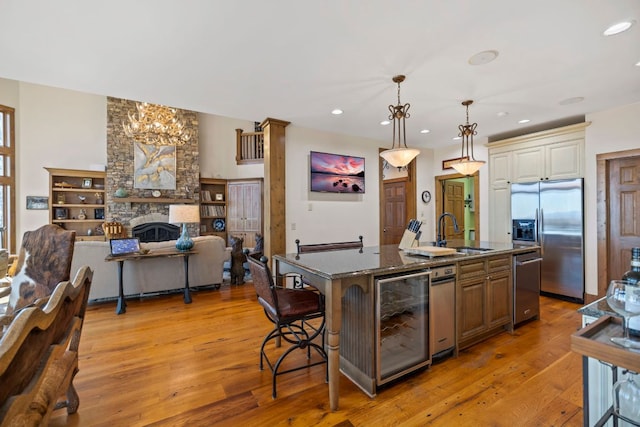 kitchen with decorative light fixtures, a sink, open floor plan, stainless steel fridge, and a center island with sink