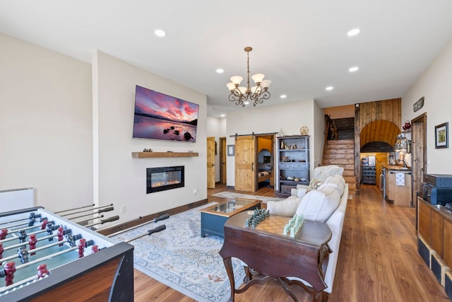 living area featuring a barn door, recessed lighting, wood finished floors, stairway, and a glass covered fireplace