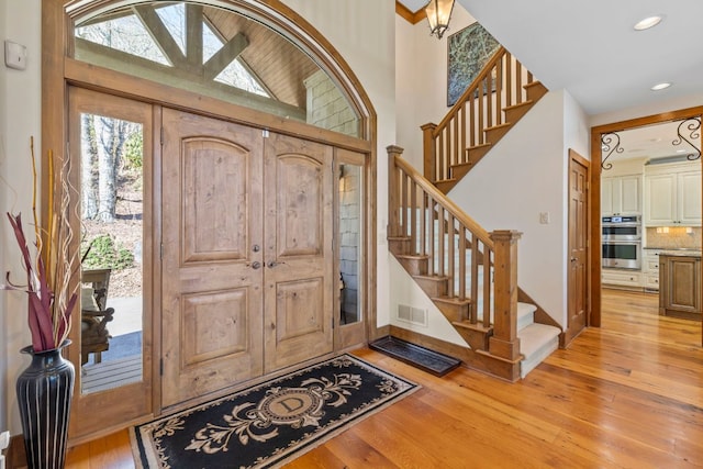 entryway with light wood-type flooring, stairs, visible vents, and a towering ceiling