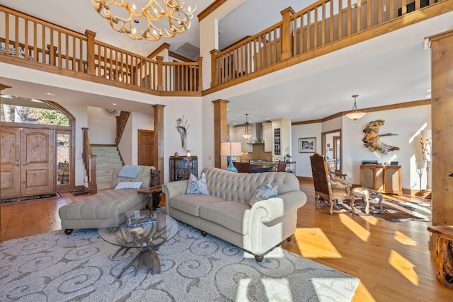 living room featuring a notable chandelier, light wood-style floors, ornamental molding, stairway, and ornate columns