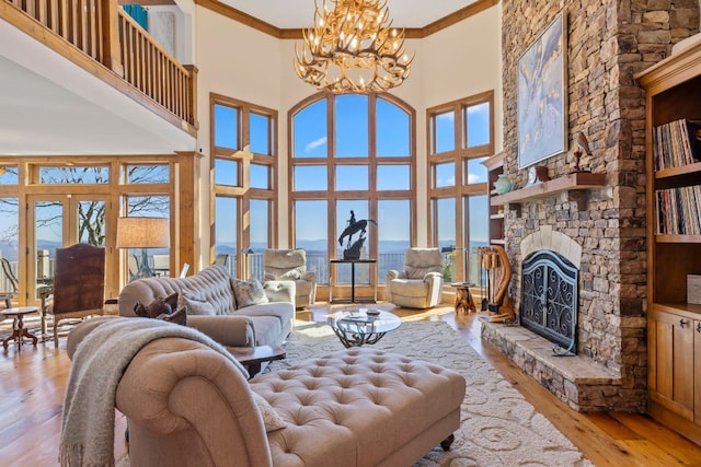 living area with crown molding, a towering ceiling, a stone fireplace, a chandelier, and light wood-type flooring