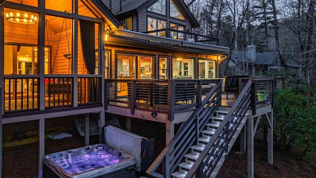 rear view of house with stairs, a wooden deck, and a hot tub