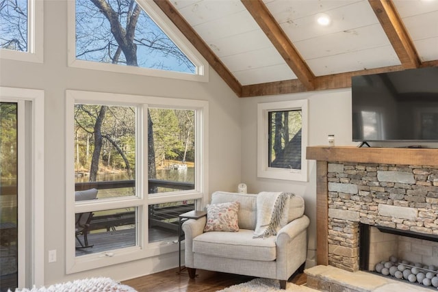 living area with lofted ceiling with beams, plenty of natural light, wood finished floors, and a stone fireplace