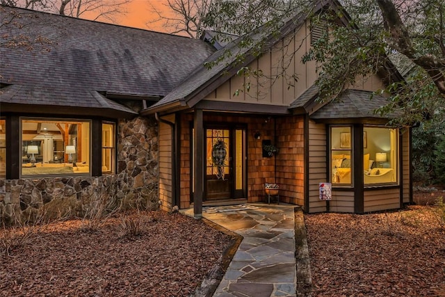 property entrance featuring stone siding, a shingled roof, and board and batten siding