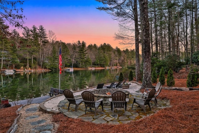 patio terrace at dusk featuring an outdoor fire pit, a water view, and a forest view