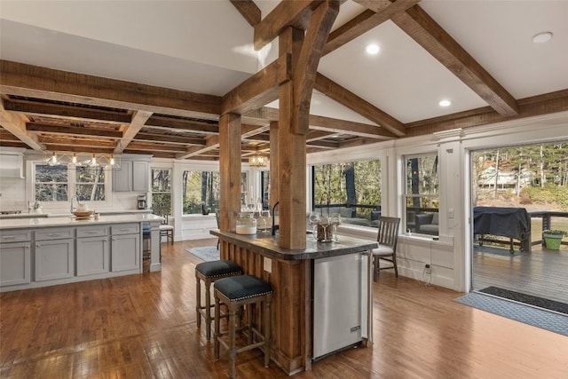 kitchen featuring dark wood finished floors, beamed ceiling, refrigerator, gray cabinetry, and a kitchen bar