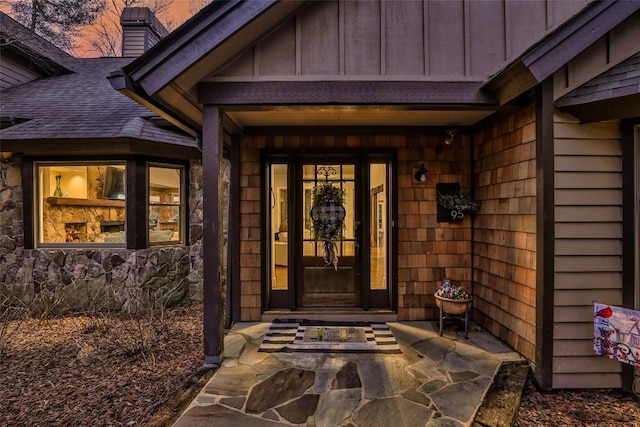 property entrance featuring stone siding, a shingled roof, board and batten siding, and a chimney