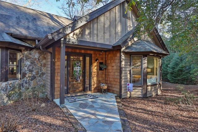 entrance to property featuring board and batten siding, stone siding, and roof with shingles