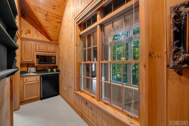 kitchen featuring wood ceiling, vaulted ceiling, black microwave, wooden walls, and light colored carpet