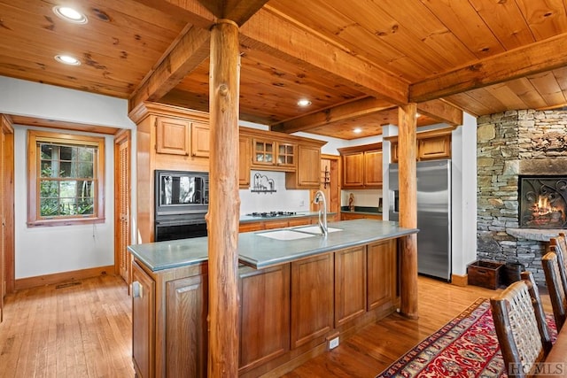 kitchen featuring beam ceiling, light hardwood / wood-style floors, stainless steel fridge with ice dispenser, and a center island with sink