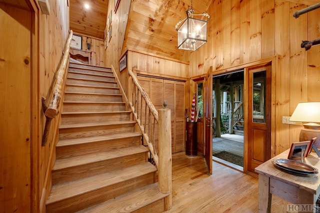 stairway with an inviting chandelier, wooden ceiling, wooden walls, hardwood / wood-style flooring, and a high ceiling