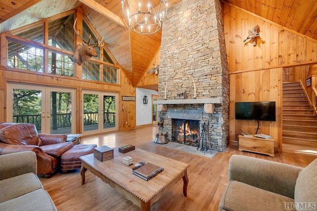 living room with high vaulted ceiling, a fireplace, light hardwood / wood-style floors, french doors, and wood walls