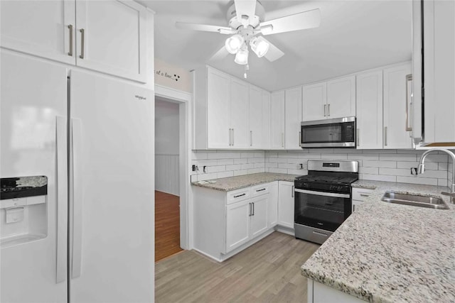 kitchen featuring appliances with stainless steel finishes, a sink, ceiling fan, light wood-style floors, and white cabinetry