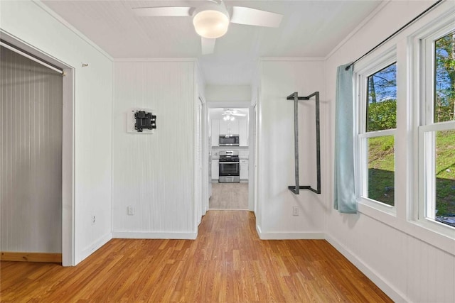 hall featuring light wood-style floors, baseboards, and crown molding