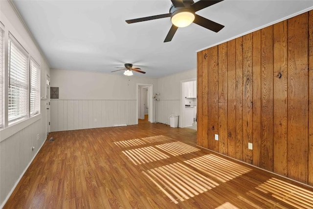 unfurnished living room featuring wood finished floors, a ceiling fan, and a wainscoted wall