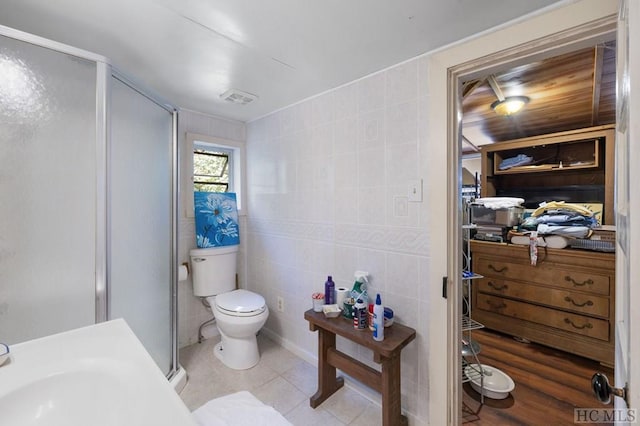 bathroom with toilet, an enclosed shower, tile patterned flooring, and tile walls