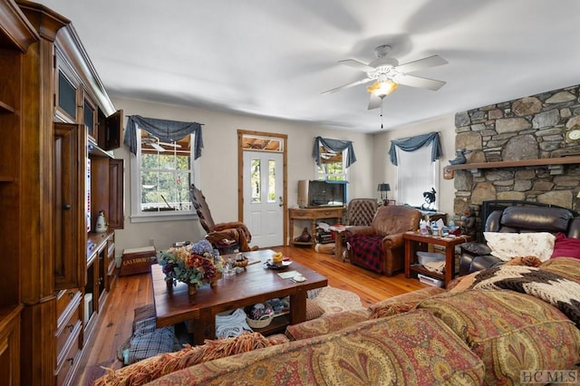 living room with ceiling fan, a stone fireplace, and light hardwood / wood-style floors