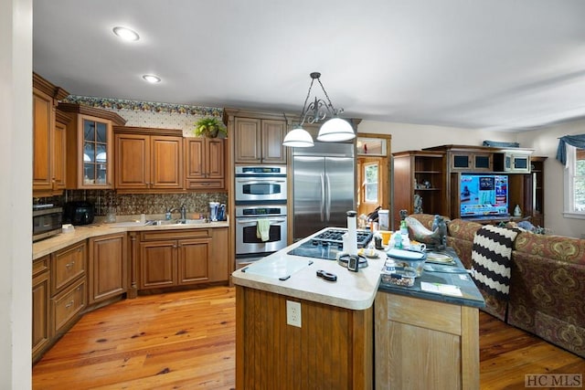 kitchen featuring sink, hanging light fixtures, stainless steel appliances, light hardwood / wood-style floors, and a kitchen island