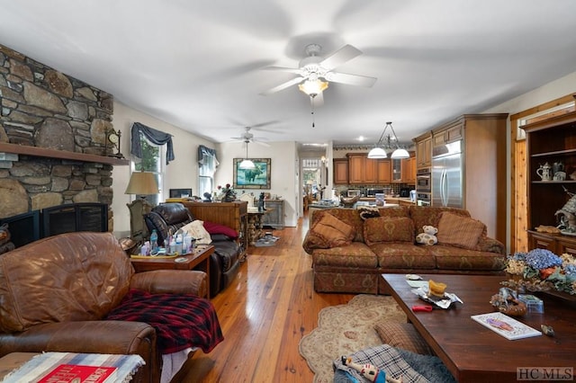 living room featuring a stone fireplace, light hardwood / wood-style floors, and ceiling fan