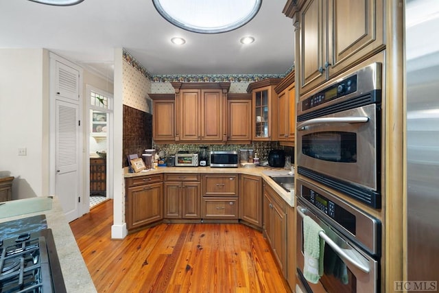 kitchen with backsplash, appliances with stainless steel finishes, sink, and light wood-type flooring