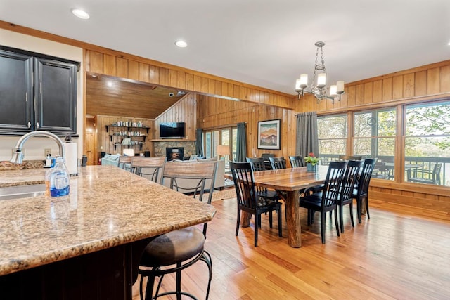 dining room with wood walls, a chandelier, light wood finished floors, a fireplace, and recessed lighting