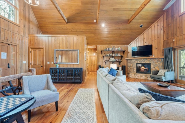 living room featuring high vaulted ceiling, wooden walls, wooden ceiling, light wood-style flooring, and a stone fireplace