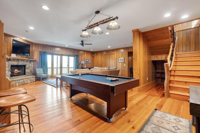 rec room with wood walls, billiards table, a stone fireplace, recessed lighting, and light wood finished floors