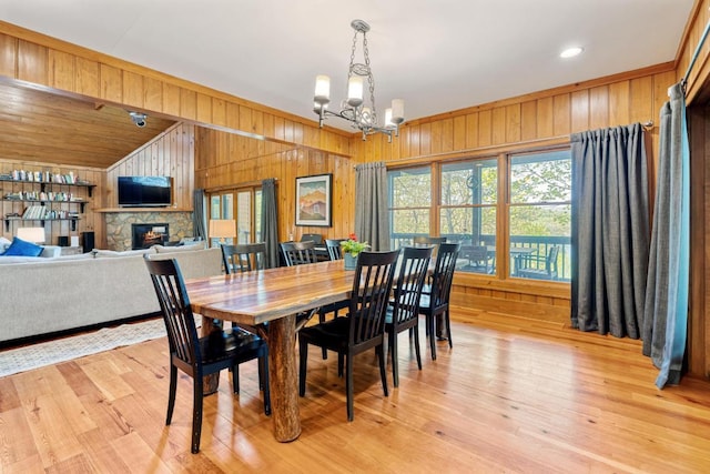 dining space featuring wood walls, healthy amount of natural light, a chandelier, a fireplace, and light wood-type flooring