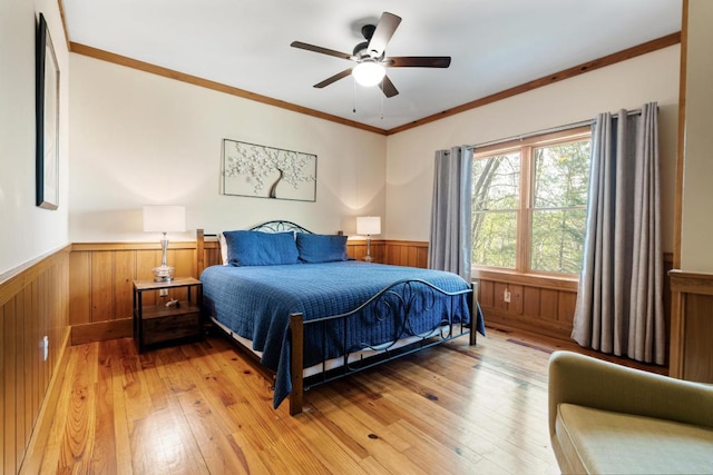 bedroom with wainscoting, light wood-style flooring, ornamental molding, wooden walls, and ceiling fan