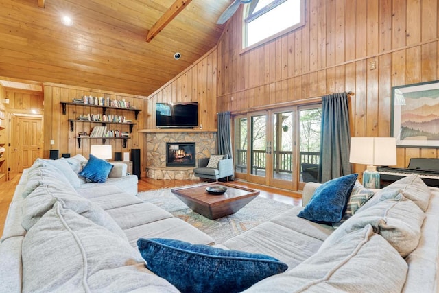 living area featuring high vaulted ceiling, healthy amount of natural light, wooden walls, a stone fireplace, and wood finished floors