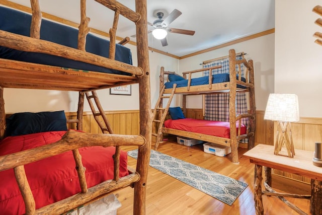 bedroom with a wainscoted wall, wood finished floors, wood walls, and crown molding
