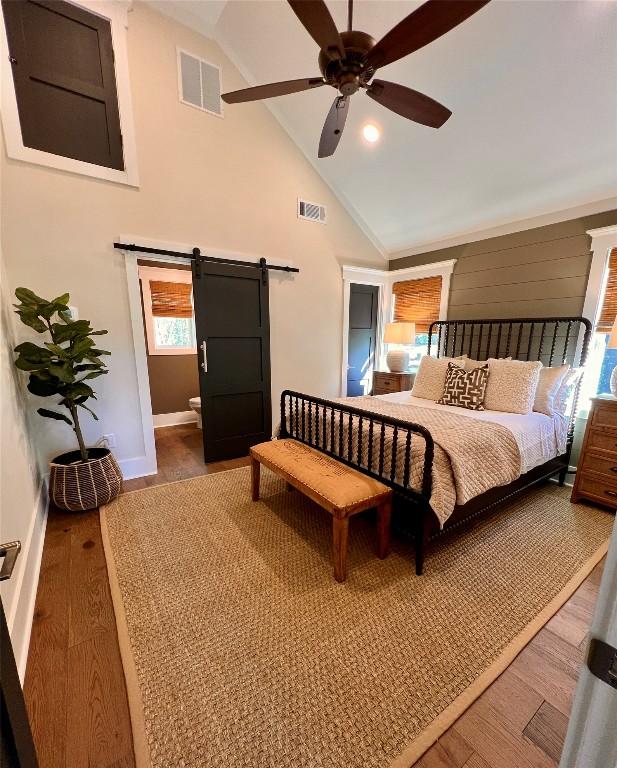 bedroom with baseboards, wood finished floors, a barn door, and visible vents