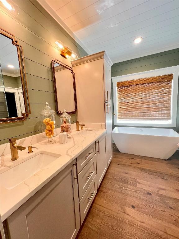 bathroom featuring double vanity, wood walls, wood finished floors, a soaking tub, and a sink