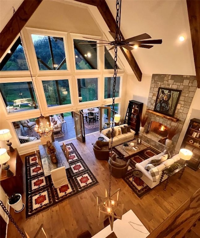 living room with wood finished floors, beam ceiling, a stone fireplace, ceiling fan, and high vaulted ceiling