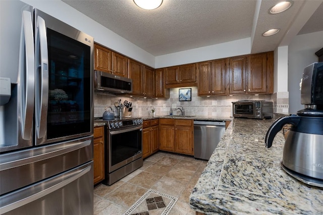 116 Fairway Villas Dr Unit D, Sapphire, NC 28774 - kitchen featuring stainless steel appliances, tasteful backsplash, light stone countertops, a textured ceiling, and brown cabinetry