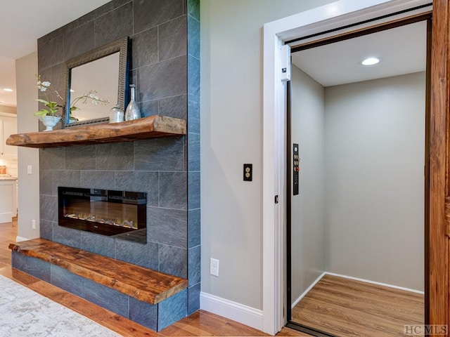 living room featuring hardwood / wood-style flooring, elevator, and a tiled fireplace