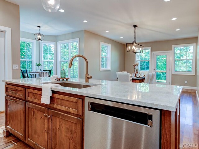 kitchen with light stone countertops, decorative light fixtures, stainless steel dishwasher, and an island with sink