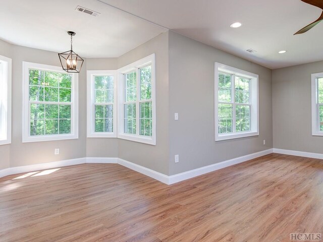 empty room with an inviting chandelier, light wood-type flooring, and plenty of natural light