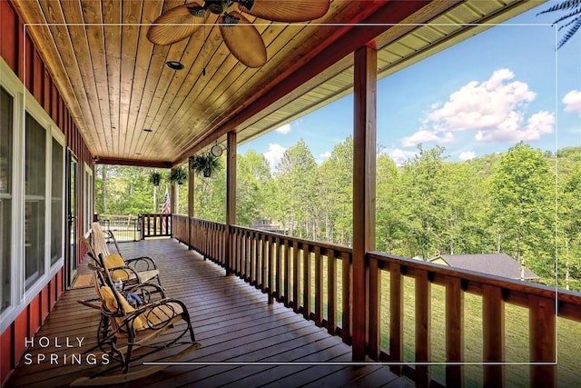 wooden deck with a porch, a ceiling fan, and a forest view