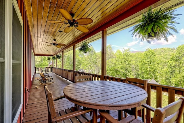 deck featuring a view of trees, a ceiling fan, and outdoor dining area