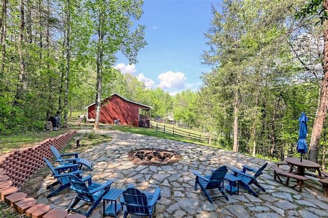 view of patio featuring a fire pit, fence, and a wooded view