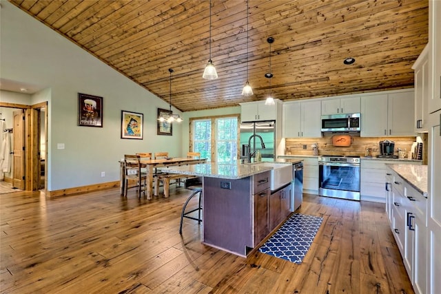 kitchen with backsplash, appliances with stainless steel finishes, a sink, white cabinets, and hardwood / wood-style floors