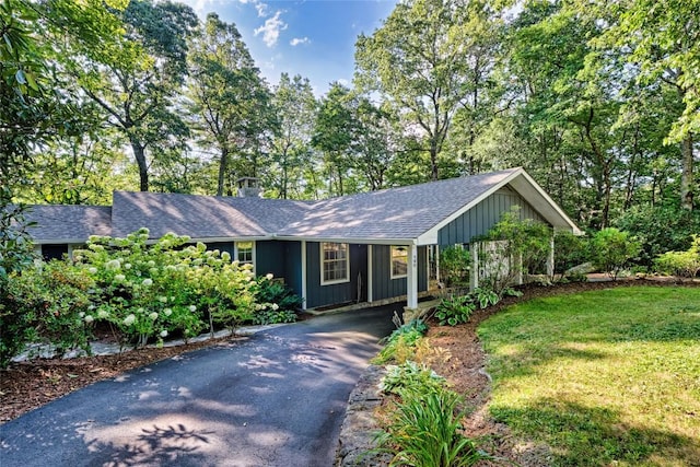 single story home featuring a front yard, a shingled roof, aphalt driveway, board and batten siding, and an attached carport